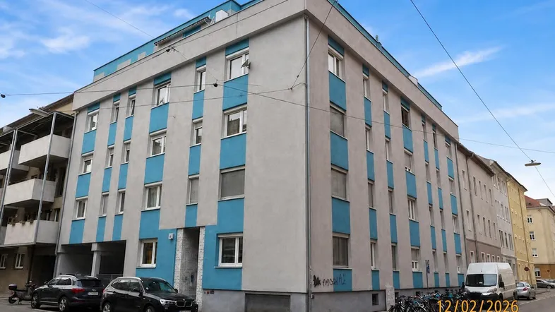 Mehrstöckiges Wohngebäude mit blauen und grauen Fassadenelementen an einer Straßenecke.