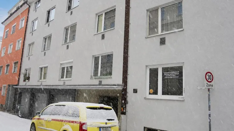 Wohngebäude im Winter mit Schnee auf der Straße und einem geparkten gelben Auto.