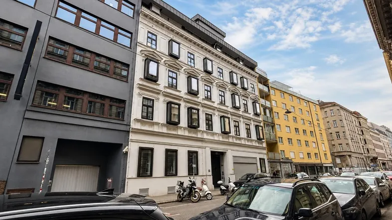 Blick auf eine belebte Stadtstraße mit geparkten Autos und einer Reihe von Gebäudefassaden.