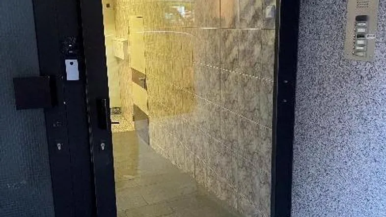 Eingangsbereich mit moderner Glastür und gefliestem Flur, der in das Gebäude führt.