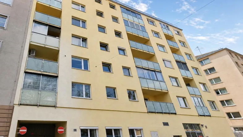 Mehrstöckiges Wohngebäude mit gelber Fassade und Balkonen unter blauem Himmel.