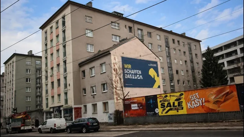 Altes Mehrfamilienhaus mit Werbetafeln an der Fassade und parkenden Autos auf der Straße.