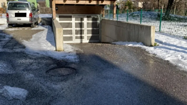 Einfahrt zu einer Tiefgarage mit Holzüberdachung und Schnee auf dem Boden.