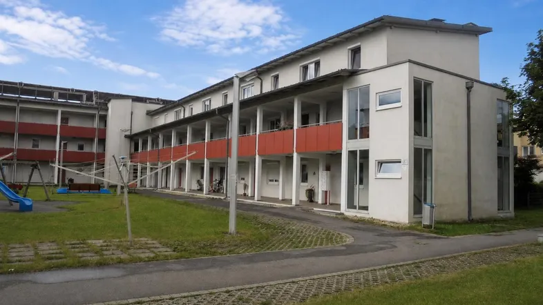 Mehrstöckiges Wohngebäude mit Balkonen, Grünfläche und Kinderspielplatz unter blauem Himmel.