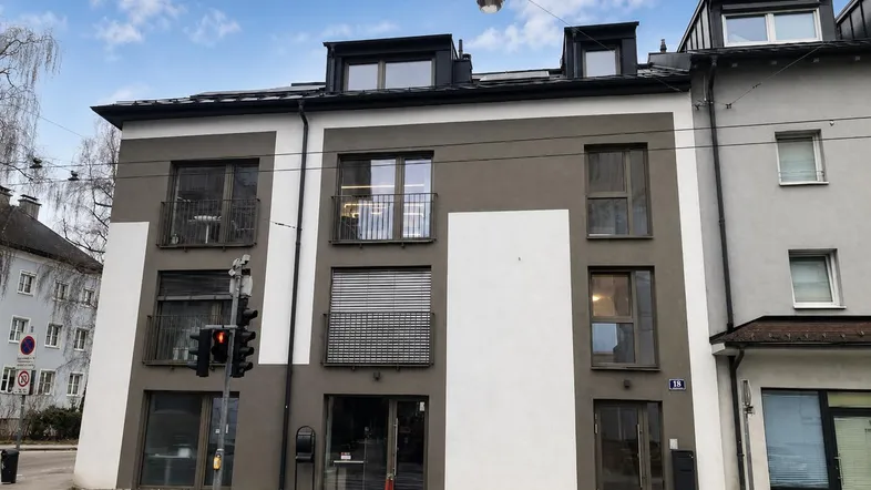 Moderne Fassade eines Mehrfamilienhauses mit Balkonen und großen Fenstern an einer Straßenecke.