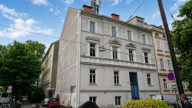 Altes Gebäude mit klassischer Fassade, vielen Fenstern und einem blauen Eingangstor an einer Straße.