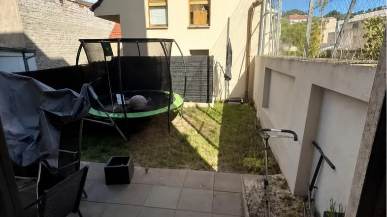 Kleiner Gartenbereich mit Trampolin, Terrasse und Rasenfläche hinter dem Haus unter blauem Himmel.