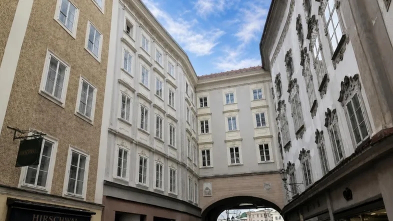 Historische Gebäude in einer engen Gasse mit einem Durchgangsbogen und blauem Himmel.