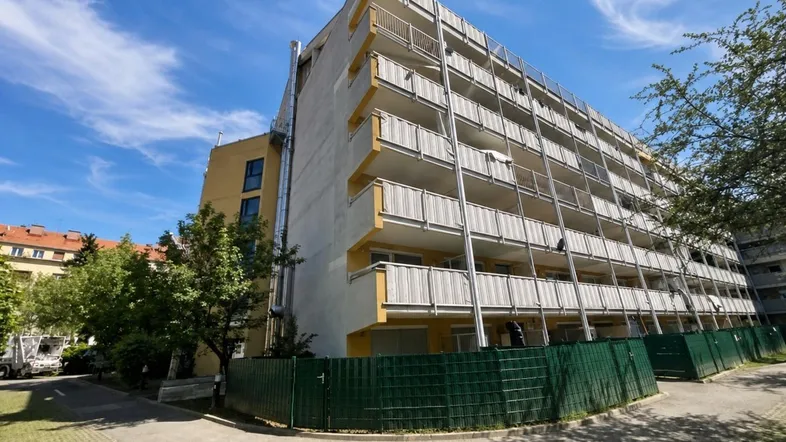 Mehrstöckiges Wohngebäude mit zahlreichen Balkonen und einer gelb-grauen Fassade unter blauem Himmel.