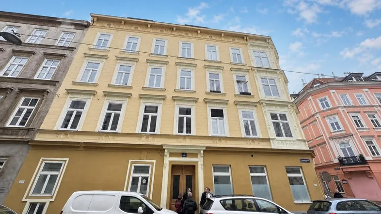Historisches Gebäude mit gelber Fassade und vielen Fenstern an einer Stadtstraße.