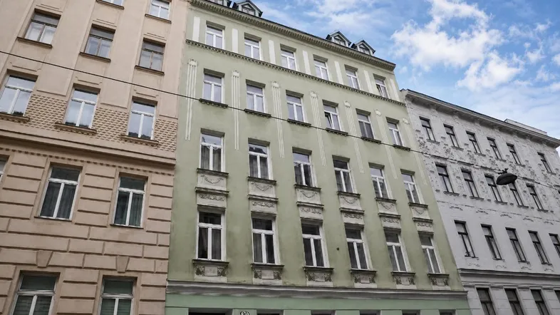 Historisches Gebäude mit hellgrüner Fassade und vielen Fenstern unter bewölktem Himmel.