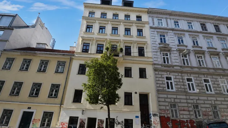 Historisches Mehrfamilienhaus mit renovierter Fassade und modernen Dachaufbauten in städtischer Umgebung.