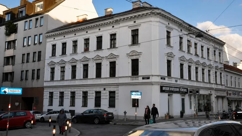 Weißes Eckgebäude in städtischer Umgebung mit klassischer Architektur und Geschäften im Erdgeschoss.