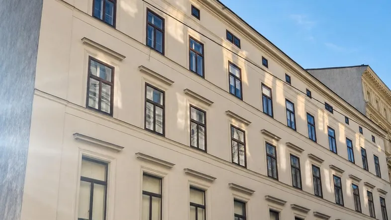 Die Fassade eines mehrstöckigen Wohngebäudes mit zahlreichen Fenstern unter blauem Himmel.