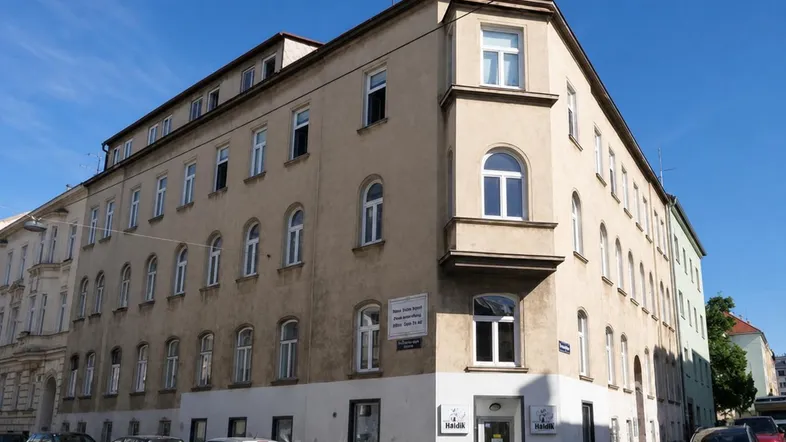 Altes Eckgebäude mit mehreren Fenstern und Geschäften im Erdgeschoss an einer Straße.