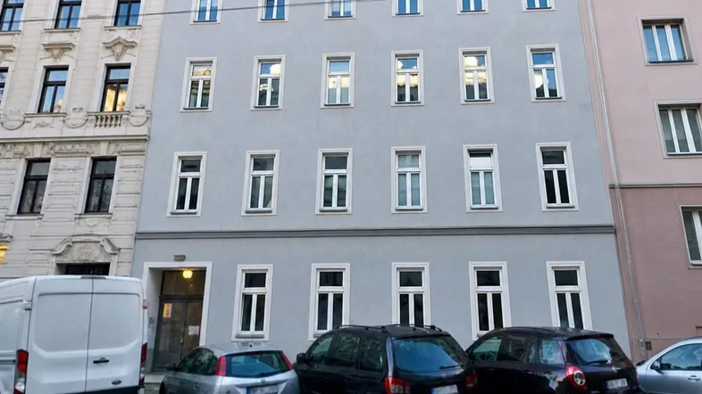 Ansicht der modernen Fassade eines Mehrfamilienhauses mit vielen Fenstern und parkenden Autos davor.