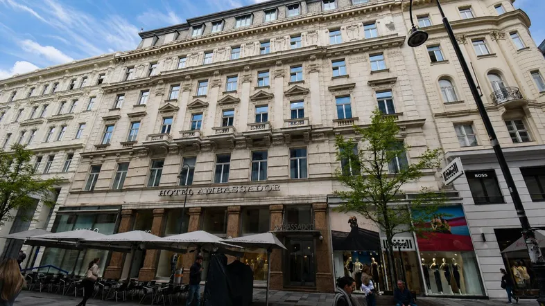 Klassisches Gebäude mit historischer Fassade und Straßencafé in einer städtischen Umgebung.