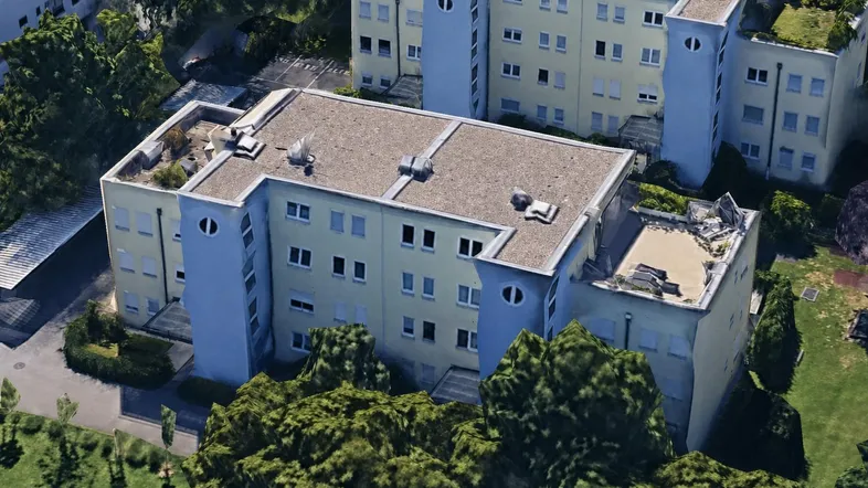 Luftaufnahme eines Wohngebäudekomplexes mit Flachdächern und umliegender Grünfläche.