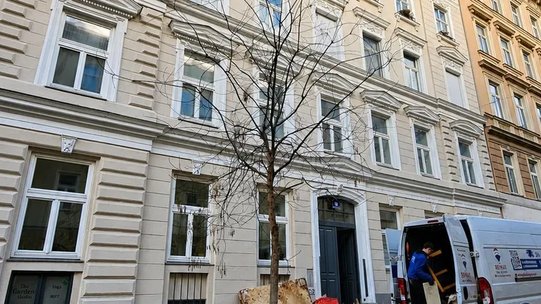 Historische Fassade eines Mehrfamilienhauses mit vielen Fenstern und einem Lieferwagen davor.