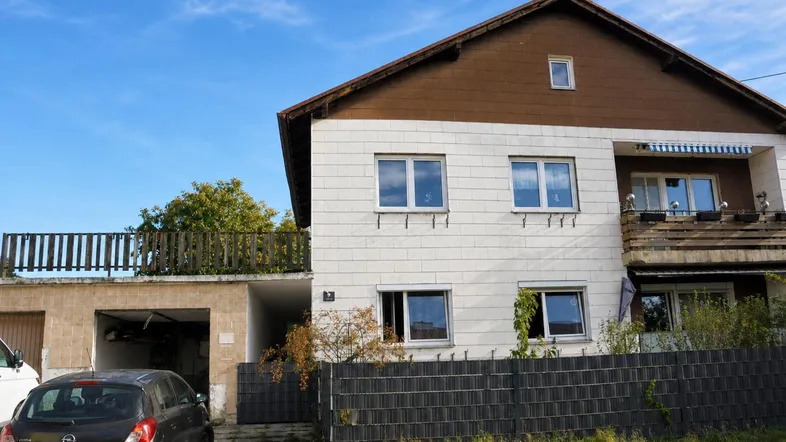 Einfamilienhaus mit weißer Fassade, braunem Dach und integrierter Garage unter blauem Himmel.