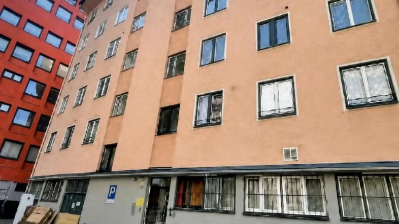 Fassade eines Mehrfamilienhauses mit orangefarbener Putzfassade und vielen Fenstern, umgeben von Bäumen.