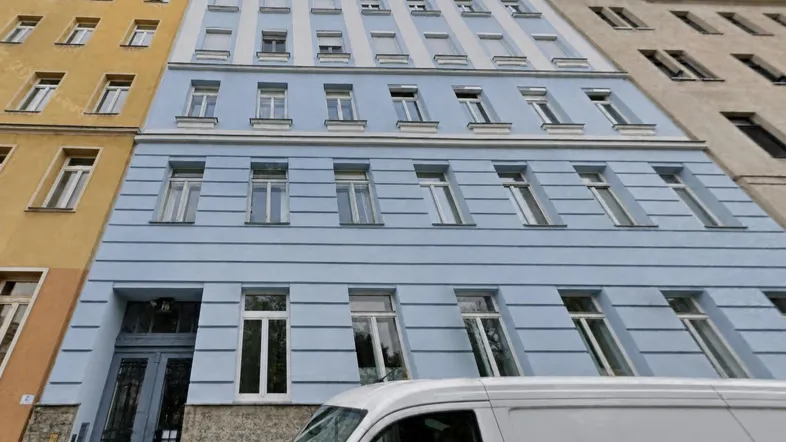 Mehrstöckiges Gebäude mit hellblauer Fassade und vielen Fenstern an einer Straße.