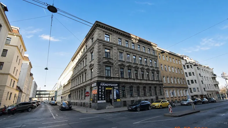Historisches Gebäude an einer Straßenecke in der Stadt, umgeben von anderen Gebäuden und Fahrzeugen.