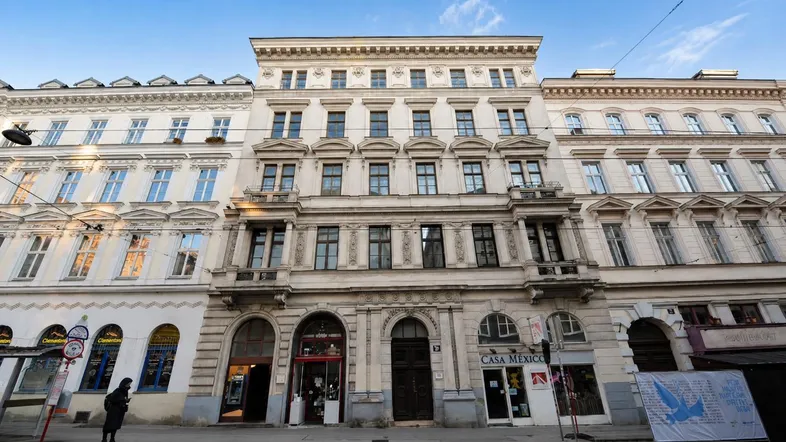 Historische Fassade eines Mehrfamilienhauses in der Stadt mit Geschäften im Erdgeschoss und kleinen Balkonen.