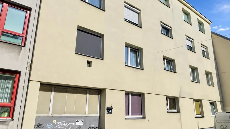 Fassade eines Mehrfamilienhauses mit hellgelbem Putz, modernen Fenstern und Rollläden.