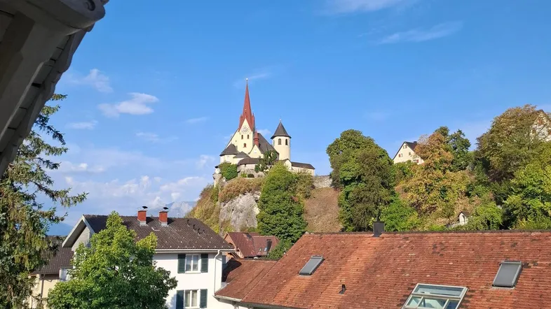 Malerischer Ausblick auf ein Dorf mit einer Kirche auf einem Hügel unter blauem Himmel.