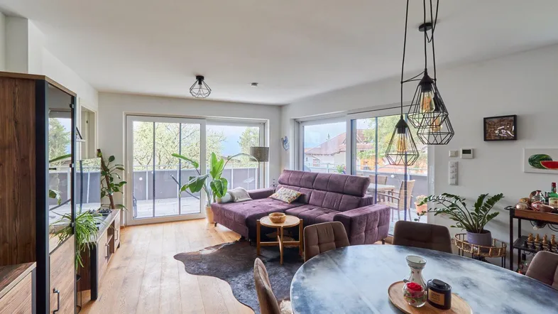 Heller Wohn-Essbereich mit Parkettboden, gemütlichem Sofa und Zugang zum großen Balkon.