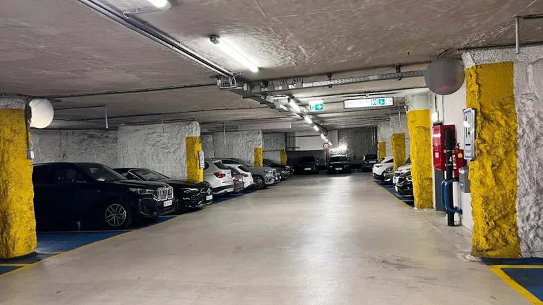 Geräumige Tiefgarage mit mehreren geparkten Fahrzeugen und rauen, gelb gestrichenen Pfeilern.