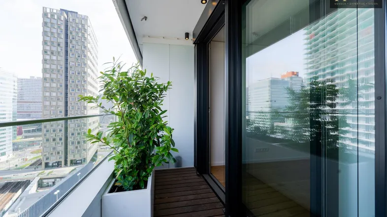 Moderner Balkon mit Holzfußboden und Glasgeländer, bietet einen urbanen Ausblick auf die Stadt.