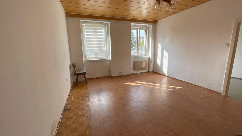 Geräumiges Zimmer mit Parkettboden, Holzdecke und zwei Fenstern, bereit zur Renovierung.