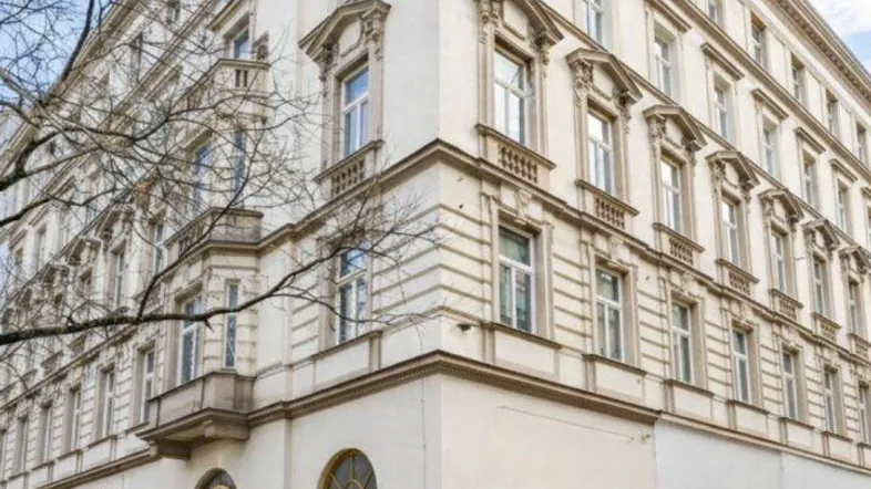 Klassisches Eckgebäude mit historischer Fassade, großen Fenstern und kleinen Außensitzbereichen auf dem Bürgersteig.