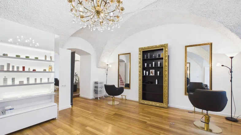 Heller Gewerberaum mit hohen Gewölbedecken, Holzboden und eleganten Friseurstühlen und Regalen.
