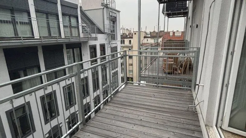 Geräumiger Balkon mit Holzboden und Metallgeländer, der einen Blick auf die umliegenden Stadtgebäude bietet.