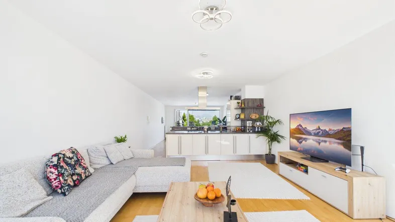 Helles, offenes Wohnzimmer mit integrierter Küche, Parkettboden und modernem Mobiliar.