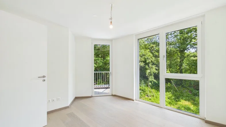 Helles Zimmer mit großen Fenstern, Holzboden und Zugang zu einem kleinen Balkon.