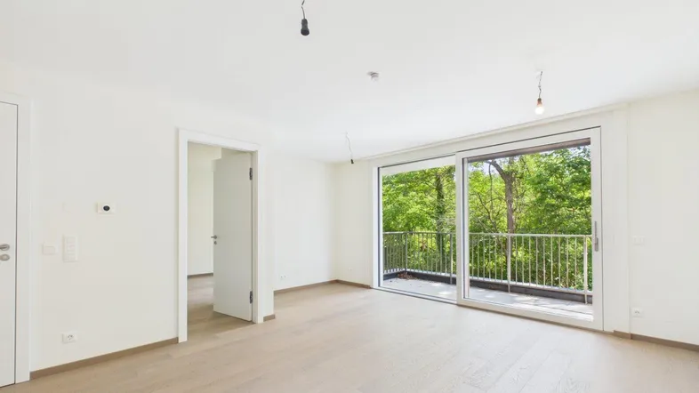 Heller Wohnbereich mit Holzboden und Zugang zu einem Balkon mit Blick ins Grüne.