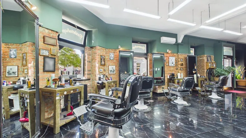 Geräumiger Friseursalon mit mehreren Bedienplätzen, schwarzen Marmorböden und industriellem Design.