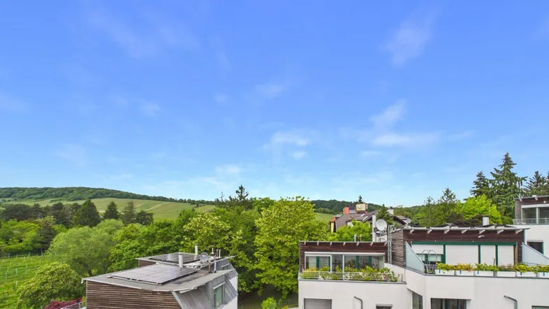 Panoramablick über moderne Gebäude, grüne Hügel und Weinberge unter blauem Himmel.