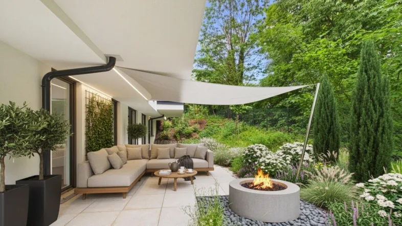 Großzügige Terrasse mit bequemen Loungemöbeln, Feuerstelle und üppiger Bepflanzung im Grünen.