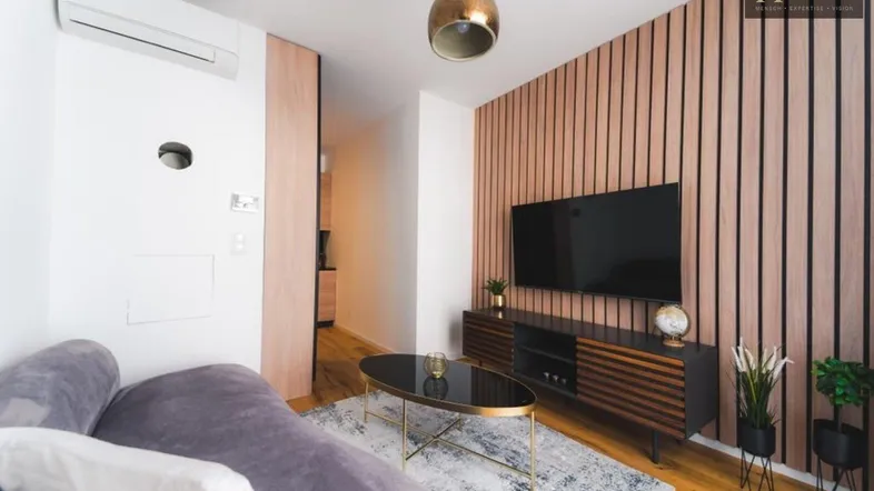 Modernes Wohnzimmer mit Holzlamellenwand, bequemer Couch und Flachbildfernseher.