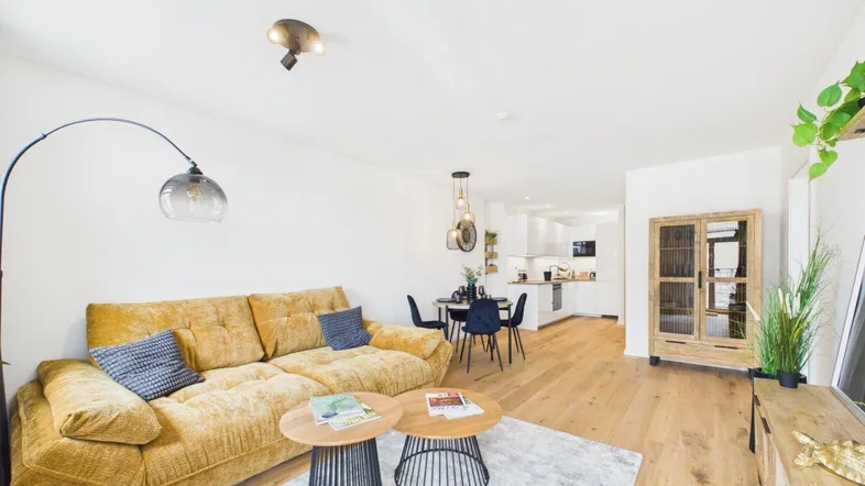 Heller offener Wohn- und Essbereich mit gelbem Sofa, Holzboden und integrierter Küche.