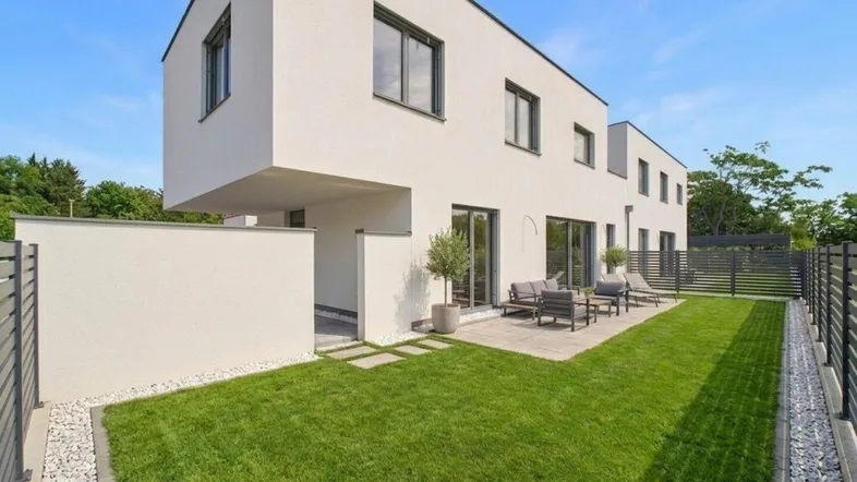 Moderne Reihenhausfassade mit gepflegtem Rasen, Terrasse und Sitzgelegenheiten im Freien.