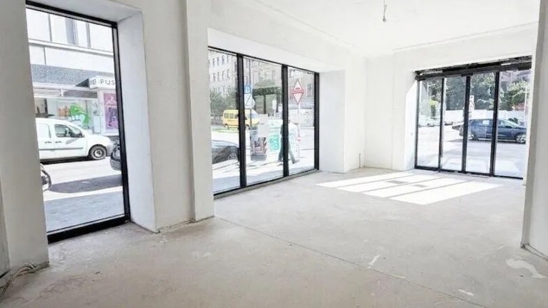 Geräumiger, unfertiger Laden- oder Büroraum mit großen Fenstern zur Straße hin, ideal für Renovierung.