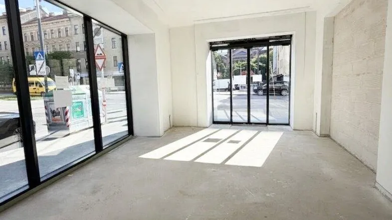 Heller Gewerberaum mit großen Schaufenstern und Betonboden, bereit für den Innenausbau.