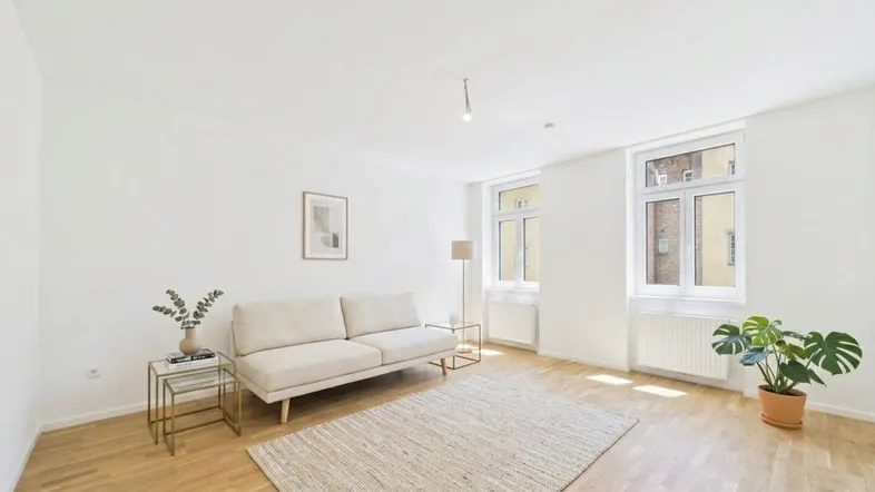 Helles Wohnzimmer mit modernem Sofa, Holzboden und großen Fenstern, die viel Tageslicht hereinlassen.