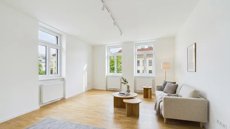 Helles Wohnzimmer mit Holzboden, weißen Wänden und großen Fenstern, die viel Tageslicht hereinlassen.